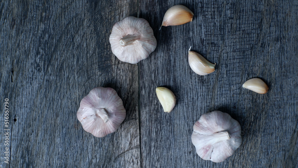 Flat lay perspective of a three garlic cloves on top rustic wood table, captured in the dark mood style.