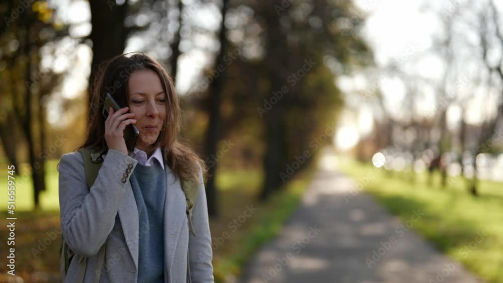 portrait of a pretty middle-aged woman talking on the phone on the street while walking in a city park portrait of a pretty middle-aged woman talking on the phone on the street while walking in a city park