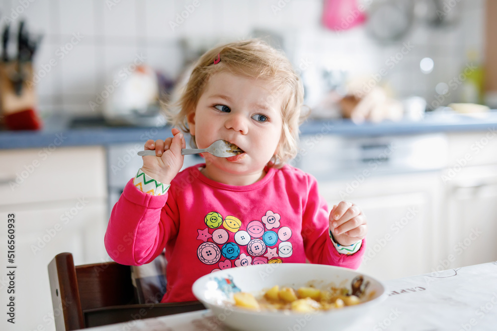 Adorable baby girl eating from fork vegetables and pasta. food, child, feeding and development concept. Cute toddler, daughter with spoon sitting in highchair and learning to eat by itself. Adorable baby girl eating from fork vegetables and pasta. food, child, feeding and development concept. Cute toddler, daughter with spoon sitting in highchair and learning to eat by itself.