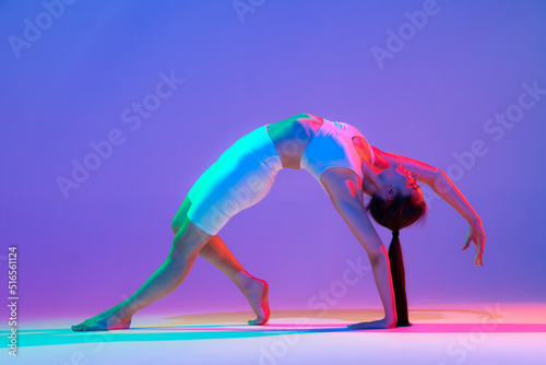 Studio shot of young flexible girl in fitness sport uniform practicing isolated on gradient pink-purple background in neon light. Sport, beauty, ad © master1305