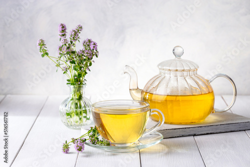 Herbal tea with thyme in a transparent cup and a bouquet of thyme on a white wooden table