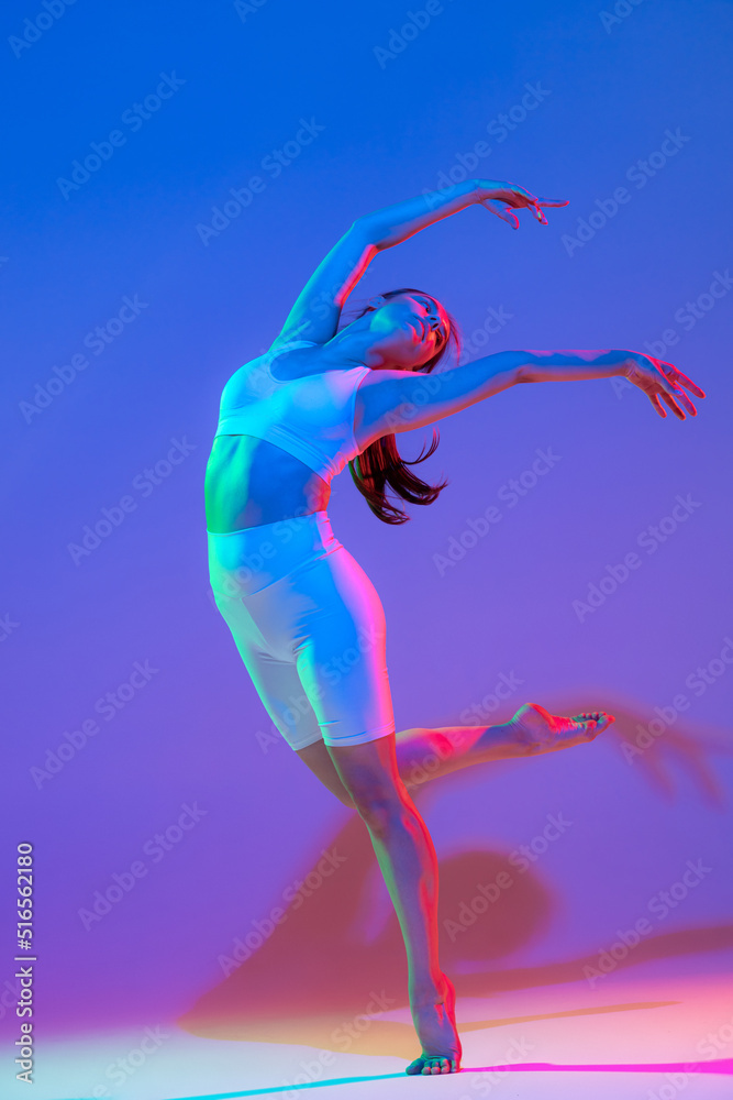 Graceful young flexible girl in fitness sport uniform dancing isolated on gradient pink-purple background in neon light. Sport, beauty, ad