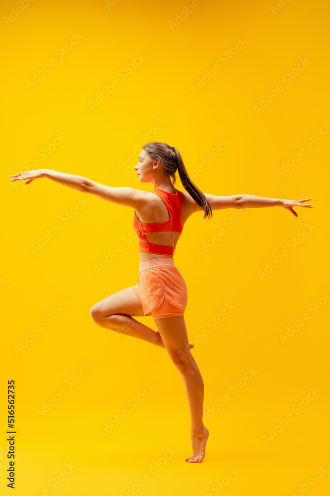 Obraz premium Young beautiful slim, flexible girl in shorts doing stretching exercises isolated on bright yellow background. Sport, health, active lifestyle
