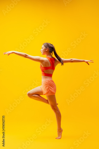 Young beautiful slim, flexible girl in shorts doing stretching exercises isolated on bright yellow background. Sport, health, active lifestyle