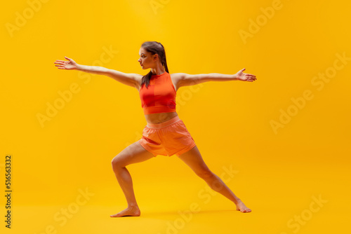 Young beautiful slim, flexible girl in shorts doing stretching exercises isolated on bright yellow background. Sport, health, active lifestyle