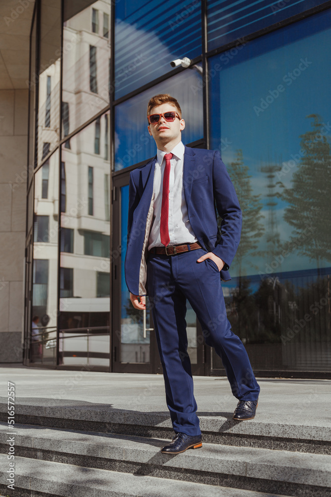 Elegant young man in blue suit and sunglasses at contemporary corporate building Elegant young man in blue suit and sunglasses at contemporary corporate building