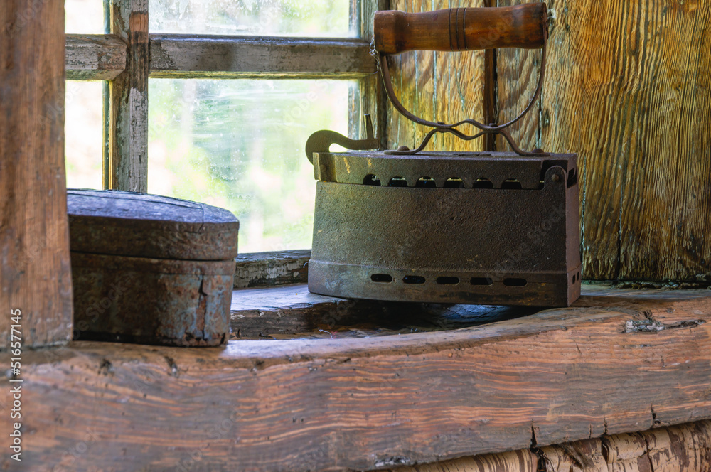 An old cast-iron coal iron made in the 19th century on the windowsill of an old wooden house. The interior of an old house. Dark log walls of the house. Rustic architecture.
