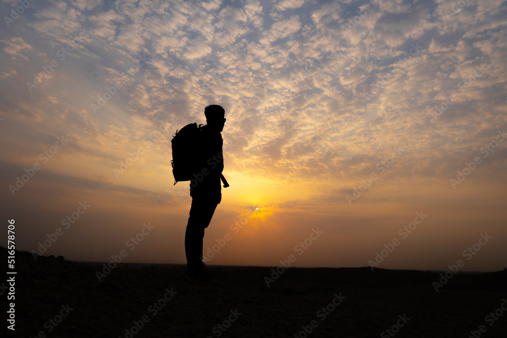 Silhouette shot of an Indian hiker staring at the sun during the sunset. Man looks at the beautiful sunset from above the hill. Natural background