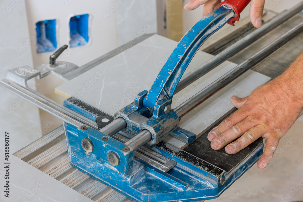 In construction worker cutting is using manual tools equipment to lay ceramic tiles on the floor during bathroom renovation In construction worker cutting is using manual tools equipment to lay ceramic tiles on the floor during bathroom renovation