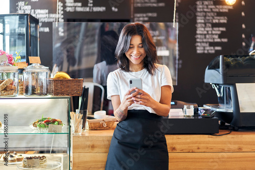 Portrait of smiling waitress barista using mobile phone at work
