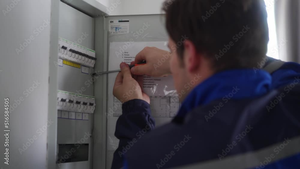 Electrician installs electrical fuse box. Master in uniform tightens screws on electrical panel with screwdriver to fix electricity. Repairman fixing domestic issues. Electrician installs electrical fuse box. Master in uniform tightens screws on electrical panel with screwdriver to fix electricity. Repairman fixing domestic issues.