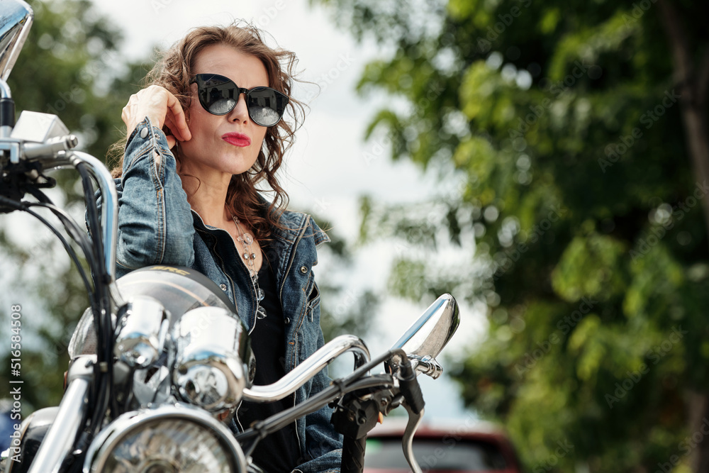 Stylish female motorcyclist with red lips taking on sunglasses