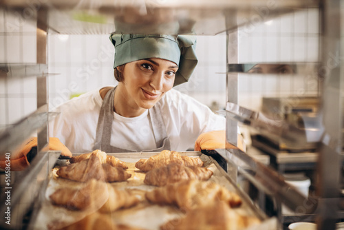 Female baker at the kitchen holding freshly baked croiisants