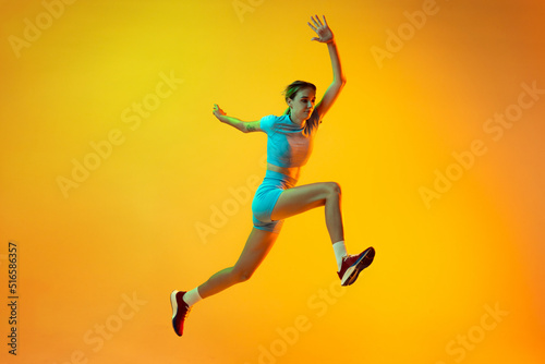 Professional longjumper. One female athlete in sports uniform jumping isolated on yellow background. Concept of sport, action, motion, speed.