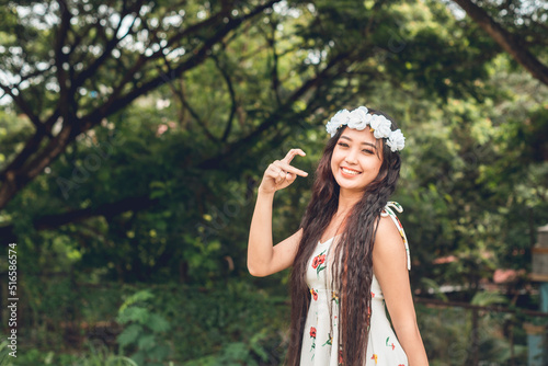 A young asian maiden in a floral dress makes a cute half heart gesture while at a park. Looking for someone to complete her love life. photo