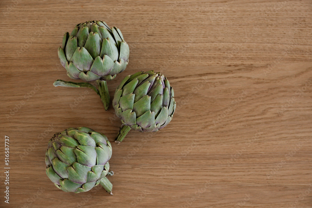 Fototapeta premium Fresh green Italian Artichoke natural wood background. Organic local produce vegetable on textured table. Vegan diet. Clean eating concept. Close up, top view, flat lay.