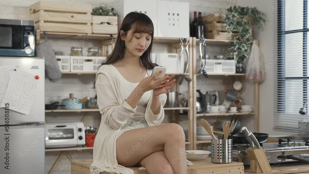 sexy chinese woman sitting on kitchen table with folded leg is checking phone messages in leisure on a tranquil morning at home.