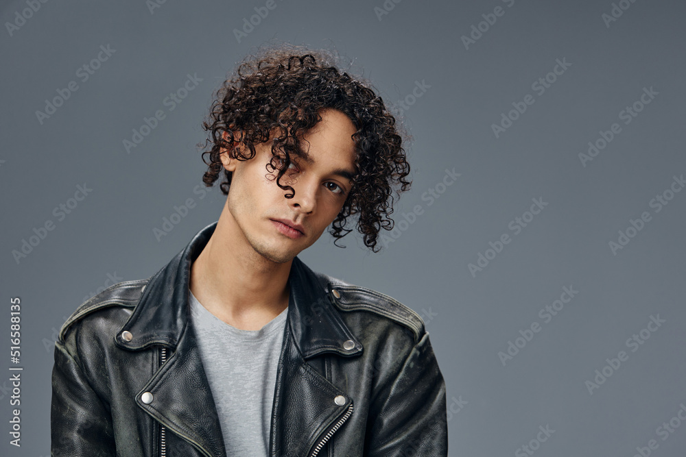Obraz premium Self-confident stylish tanned curly man leather jacket looks at camera posing isolated on over gray studio background. Cool fashion offer. Huge Seasonal Sale New Collection concept. Copy space for ad