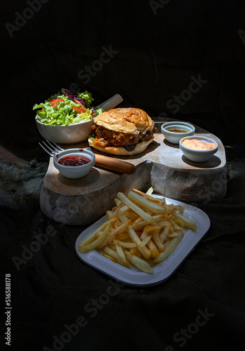Pork burger with white sesame seeds with French fries potatoes and Salad served with ketchup sauce, mayonnaise and salad dressing on wooden cutting board. The concept of delicious food, Copy space. © num