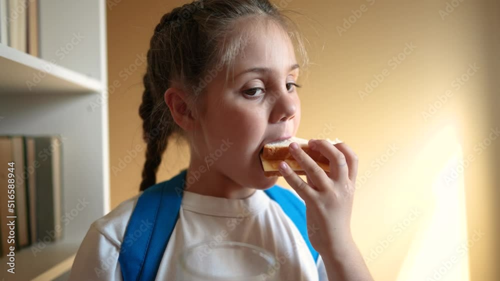 schoolgirl eats a sandwich drinking juice at school during recess with backpack and bookcase education. child lunch concept. child in classroom having lunch snack with bread and sandwich indoor schoolgirl eats a sandwich drinking juice at school during recess with backpack and bookcase education. child lunch concept. child in classroom having lunch snack with bread and sandwich indoor