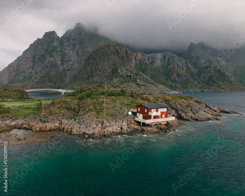 Red norwegian hut in front of the ocean with mountains and a bridge in the background