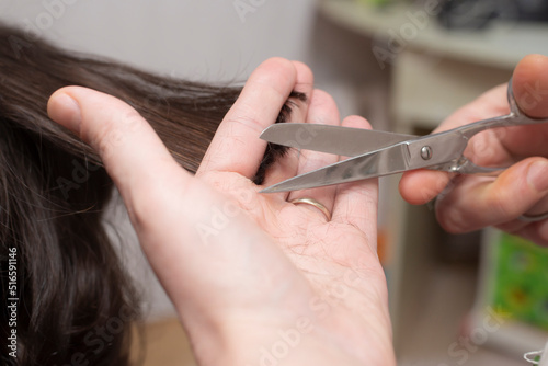 Mother's hands with scissors, trimming her son's hair at home. Soft focus close up. 