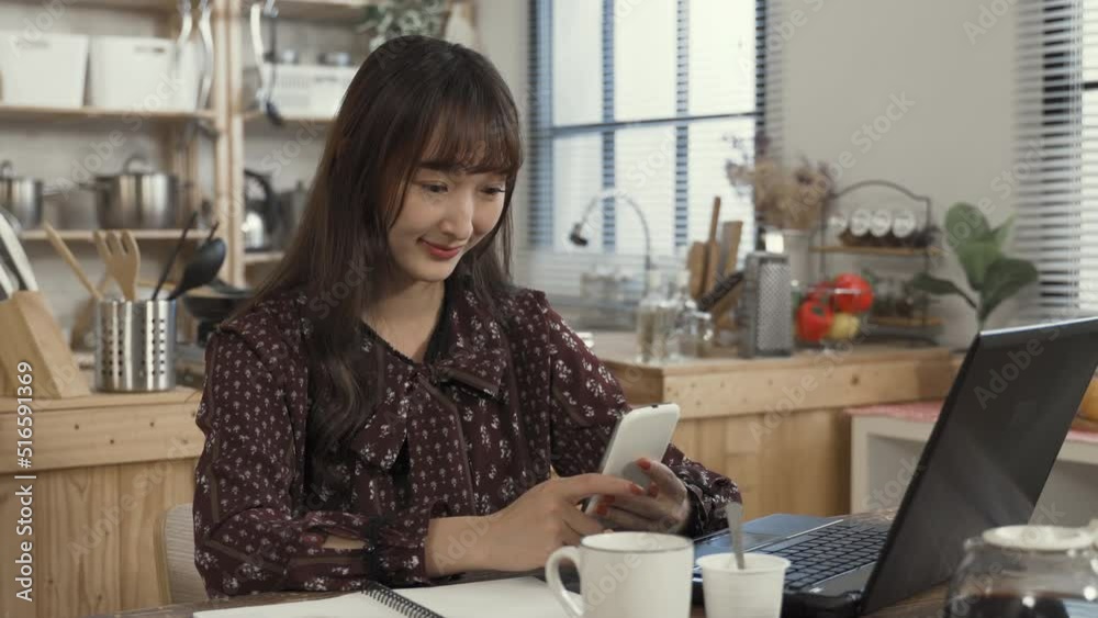 portrait of cheerful asian woman working from home is texting phone messages with a smile while taking a break at the table in the dining room. portrait of cheerful asian woman working from home is texting phone messages with a smile while taking a break at the table in the dining room.