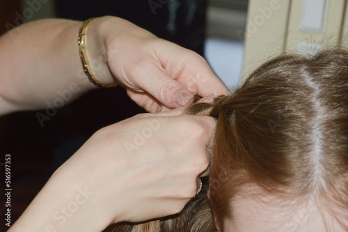 mom braids her daughter's hair. women's hands weave a braid on the girl's head.