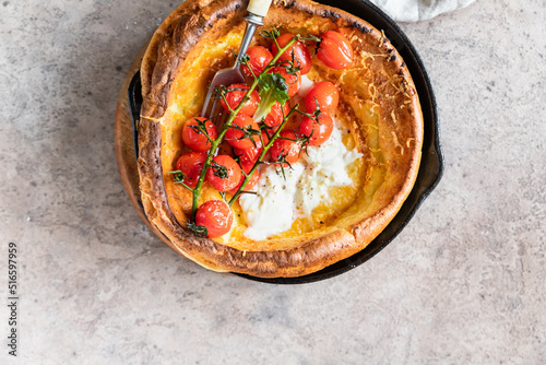 Savory Dutch baby pancake with roasted cherry tomatoes, mozzarella cheese and green salad leaves in serving cast-iron frying pan. Danish cuisine. Hearty breakfast.