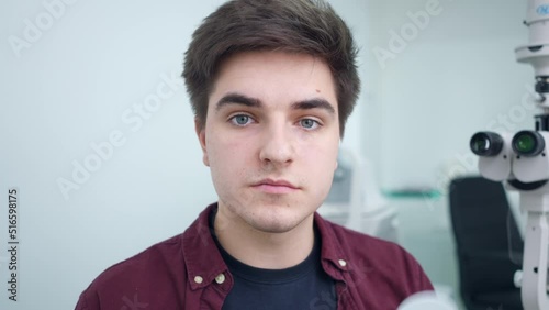 Front view man closing eyes one by one with eye occluder looking at camera. Portrait of concentrated Cauacsian patient checking eyesight in ophthalmologic clinic indoors. Health care and medicine photo