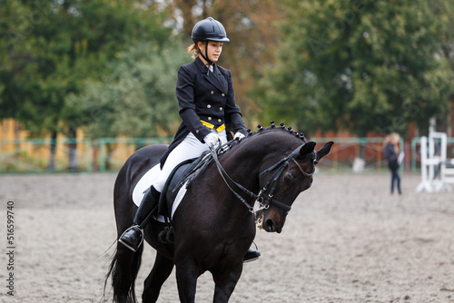 Young teenage girl riding raven horse on dressage equestrian event