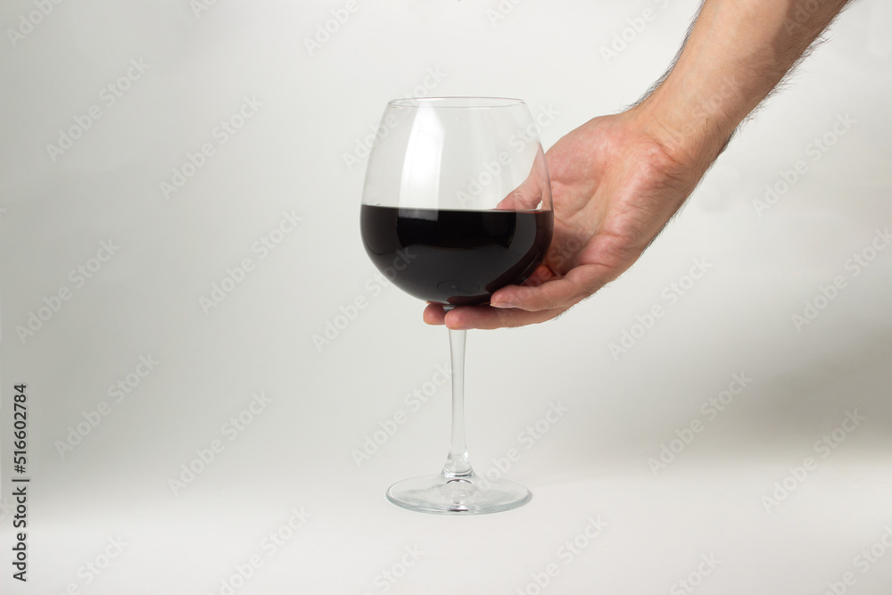A hand takes a glass of red wine on a white background. Alcoholic drink.