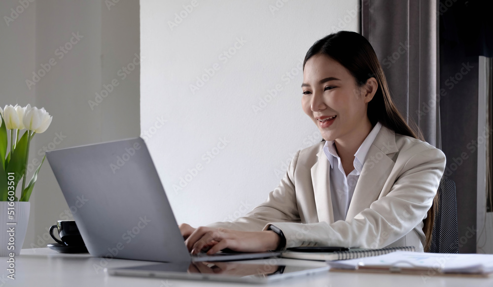 Happy young asian businesswoman sitting on her workplace in the office. Young woman working at laptop in the office. Happy young asian businesswoman sitting on her workplace in the office. Young woman working at laptop in the office.
