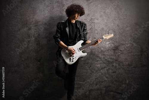 Photography Male musician in a leather jacket with an electric guitar leaning on a dark rugg
