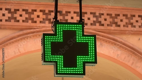  A flashing, green, LED cross as a symbol of a pharmacy, helping the sick and the needy. The concept of medicines, pandemics, rising drug prices, the quality of pharmacy products.