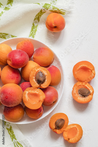 White plate with sweet orange apricots on a white table. Top view. Healthy eating with organic fruits.