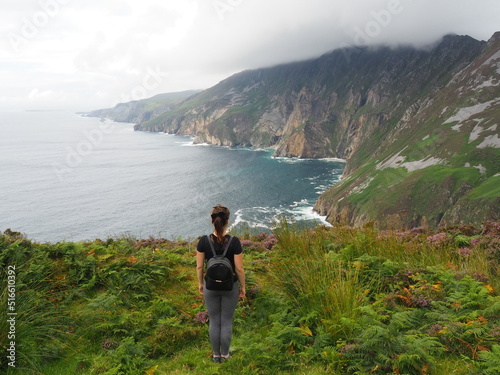 Girl looking at slieve league cliffs in Ireland with heavy clouds above cliffs