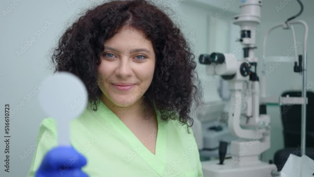 Positive intelligent doctor posing with eye occluder in ophthalmologic clinic. Portrait of smiling Caucasian woman looking at camera streching special tool standing in hospital indoors Positive intelligent doctor posing with eye occluder in ophthalmologic clinic. Portrait of smiling Caucasian woman looking at camera streching special tool standing in hospital indoors