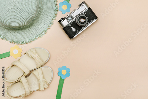 Sea beach flat lay set. Blue sun hat, women's sandals, blue and yellow flowers, retro photo camera on a beige background, copy space.