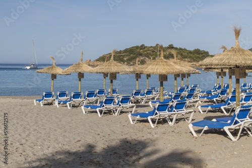 Straw umbrellas and sunbeds on a sandy beach by the sea. In the background the ship, the island. Beautiful sunny day on the Spanish coast, Europe.