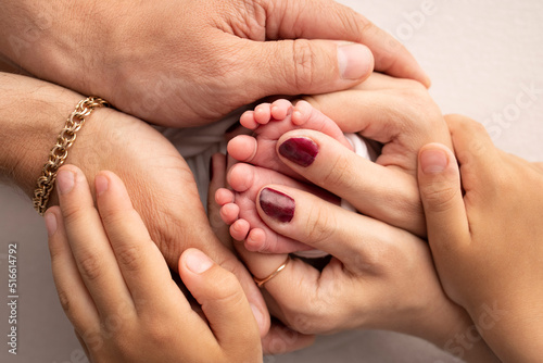 The palms of the parents, the eldest child holds the feet of the newborn child. The newborn's legs are in the hands of the mother's father and older brother and sister. Macro photo of foot, heels toes