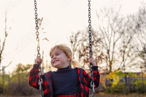 Little happy smiling child sitting on swing in park in autumn. Small girl having fun at playground. Happy childhood, freedom concept