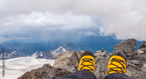 Hikers boots on mountains. First person view to legs in yellow plastic climbing boots takes a rest on the top of the mountain © Olivia
