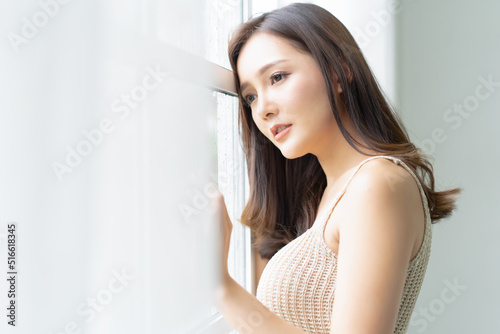 Closeup sad and depressed young Asian woman leaning at the glass window with rain drops and looking out of window at home. Sad Mood, Feel tired, Emotion, Lonely and Unhappy concept