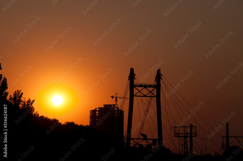Strommasten structure and construction crane silhouettes at sunset over urban landscape
