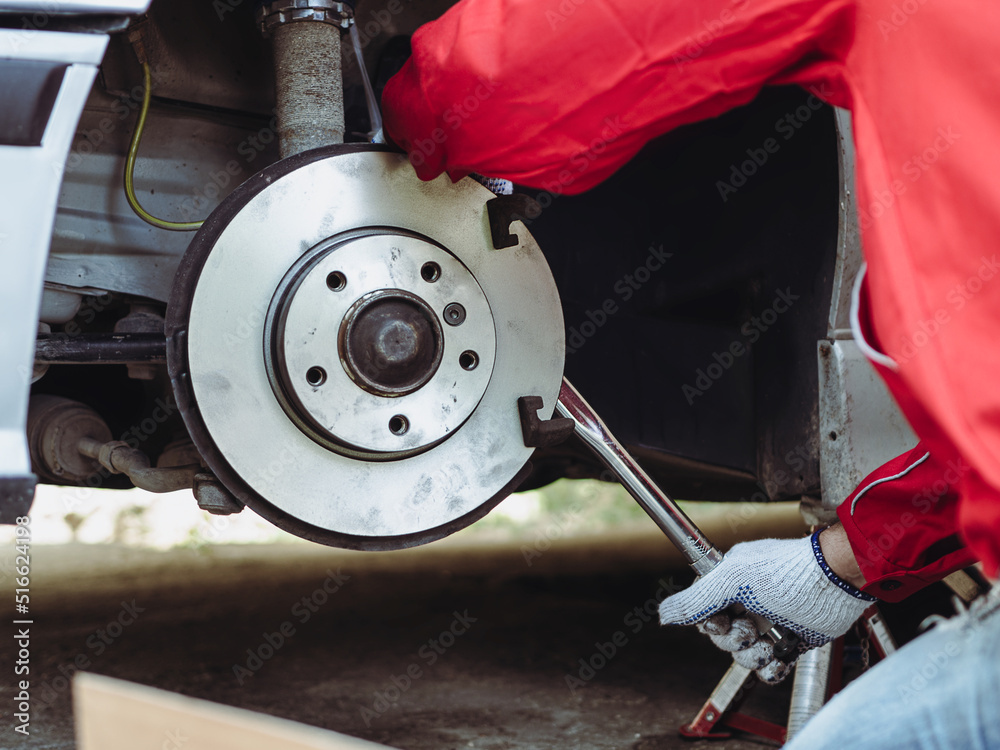 Car mechanic wearing uniform changes brake pads and use torque wrench