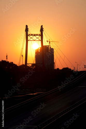 Silhouettes of electricity pylon structure  construction site and bridge road at sunset
