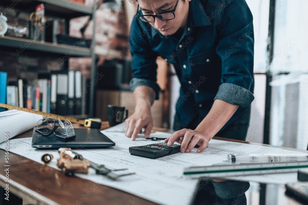 © Charnchai saeheng - Engineering working with drawings inspection on the office desk and Calculator, triangle ruler, safety glasses, compass, vernier caliper on Blueprint.