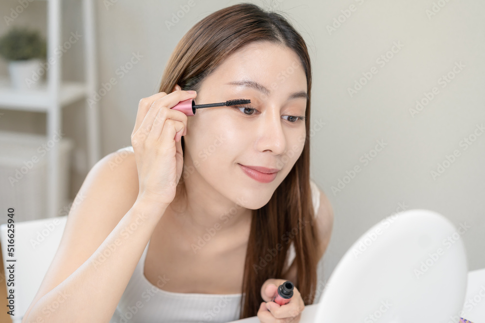 Happy beauty concept, cute asian young woman, girl smile, make up face hand by applying mascara brush on eyelash, looking into mirror in morning routine at home. People look with natural fashion style Happy beauty concept, cute asian young woman, girl smile, make up face hand by applying mascara brush on eyelash, looking into mirror in morning routine at home. People look with natural fashion style