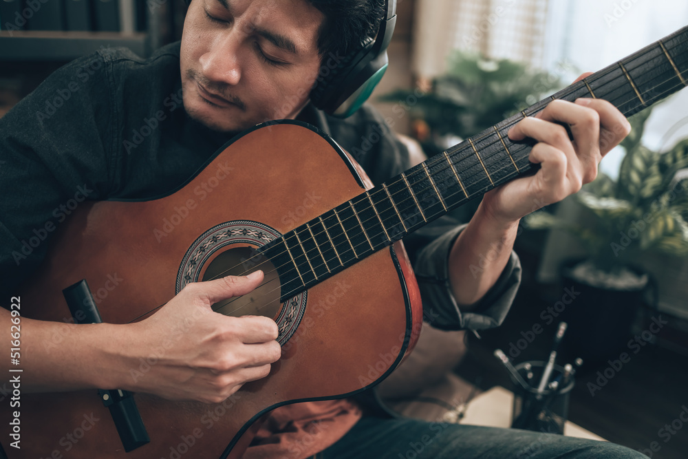 young man relax and playing guitar while sitting on sofa bed in living room at home.